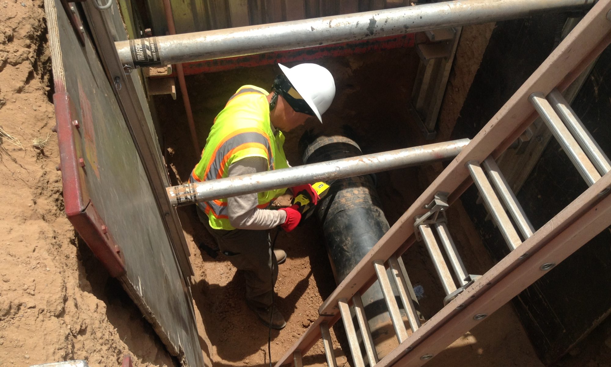 Worker inspecting a pipe in a construction trench.